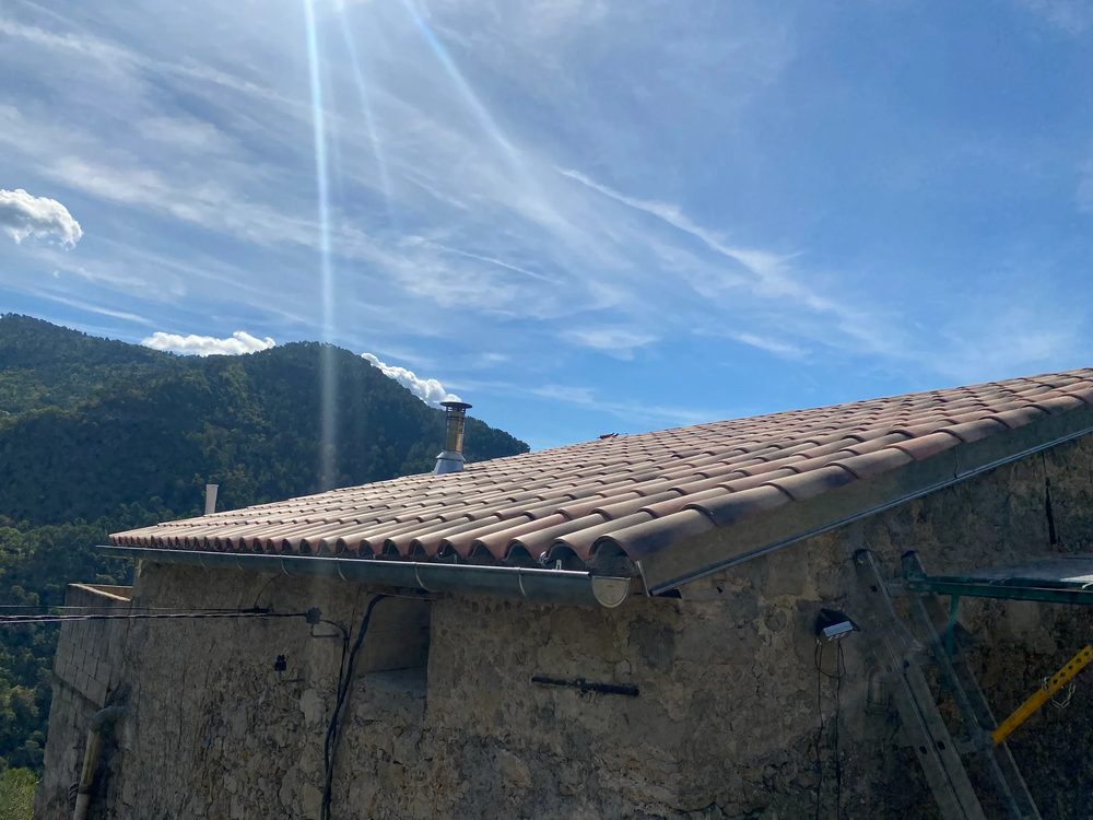 Rive de toiture ancienne en tuiles usées sur une maison en pierre, avant travaux de couverture